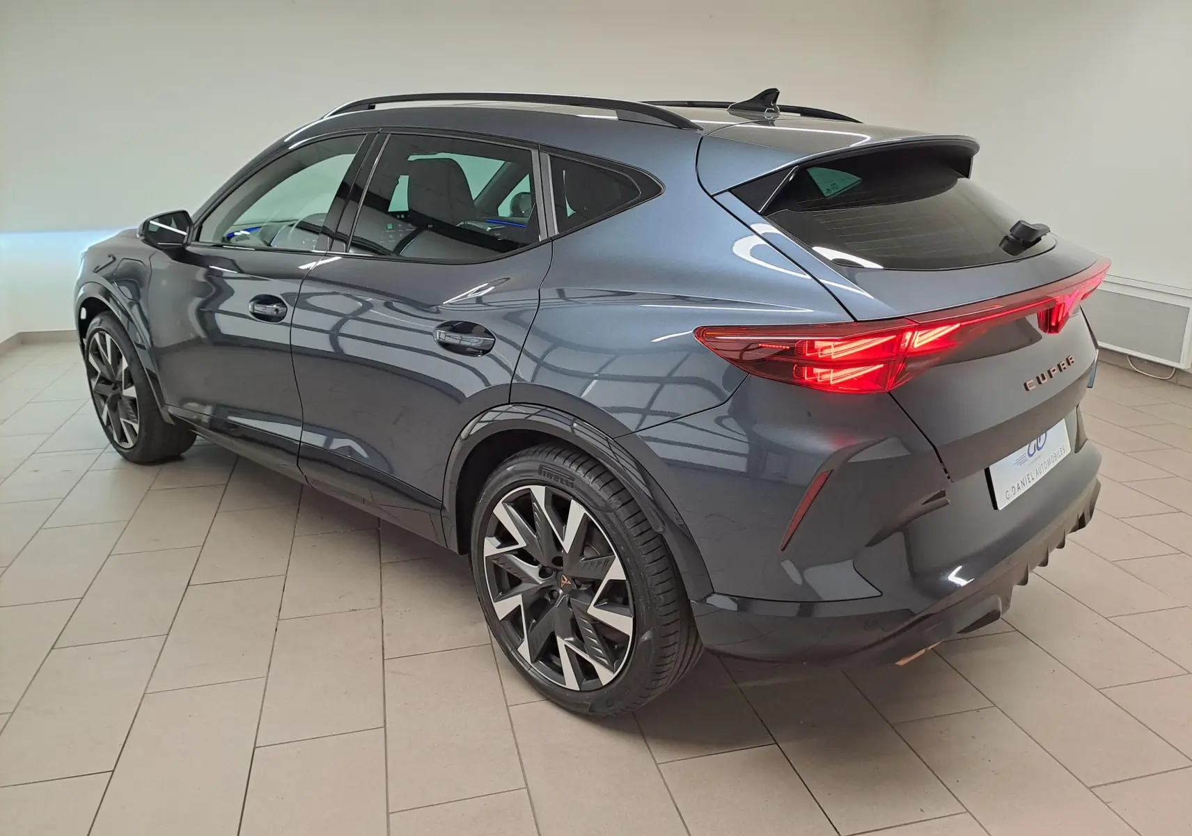 Vue 3/4 arrière droite du CUPRA Formentor gris magnétique avec feux arrière allumés et jantes alliage 19 pouces.