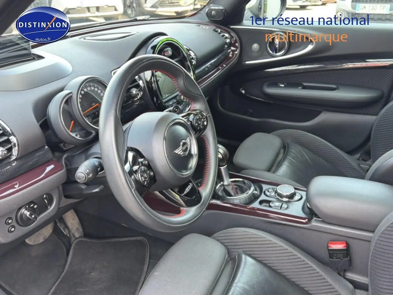 Vue intérieure côté conducteur de la MINI Clubman bordeaux, volant cuir sport et console centrale avec finitions chromées.