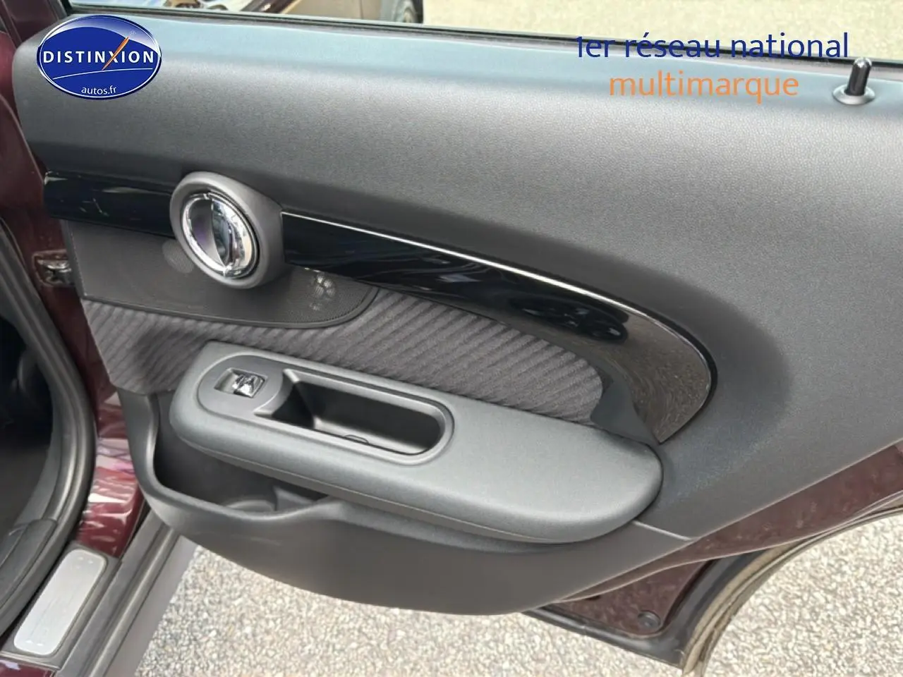 Vue rapprochée de la porte avant gauche bordeaux d'une MINI Clubman F54 avec garniture noire et poignée intégrée.