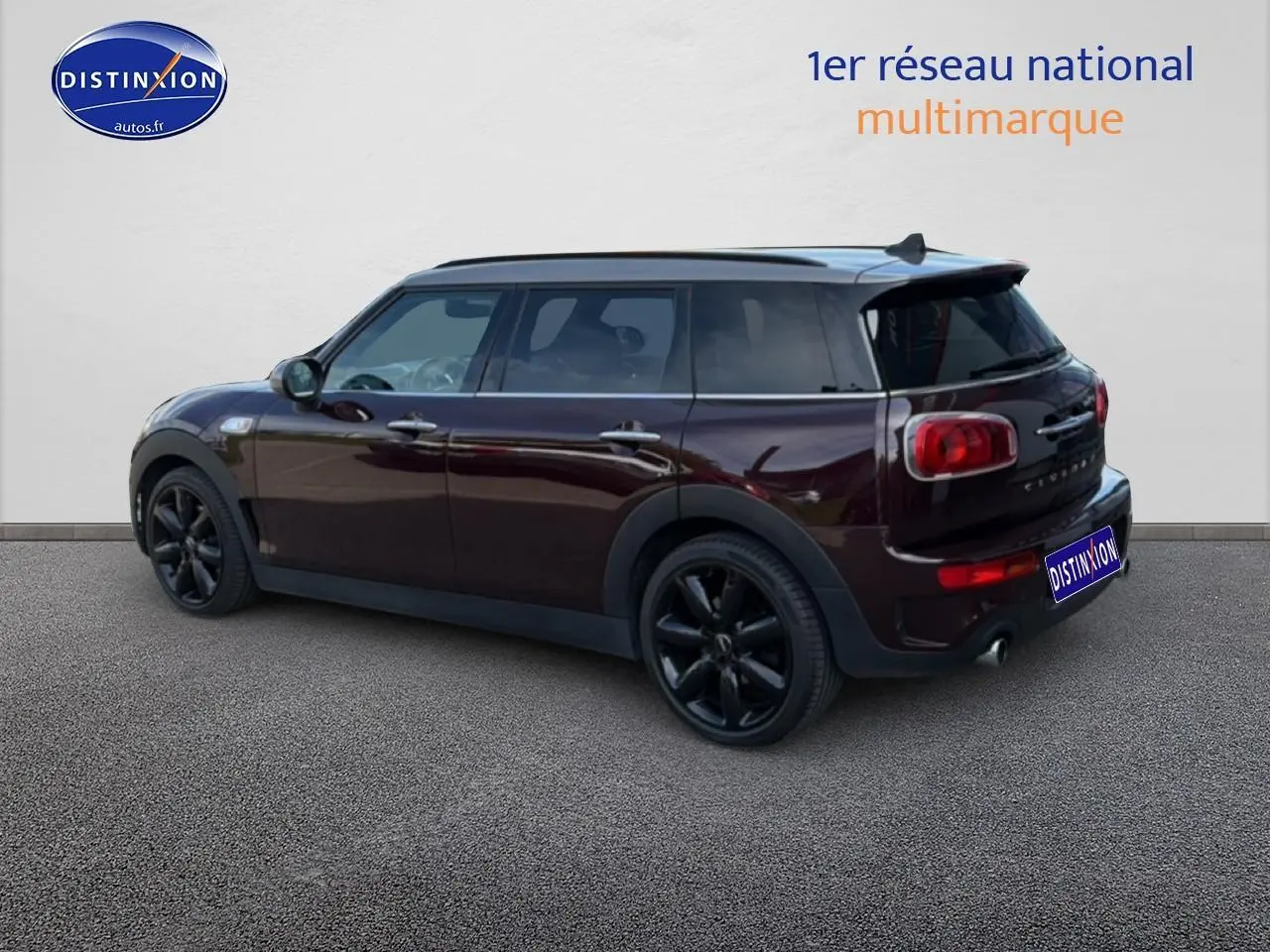 Vue 3/4 arrière droite d'une MINI Clubman bordeaux avec jantes noires et toit panoramique en verre.