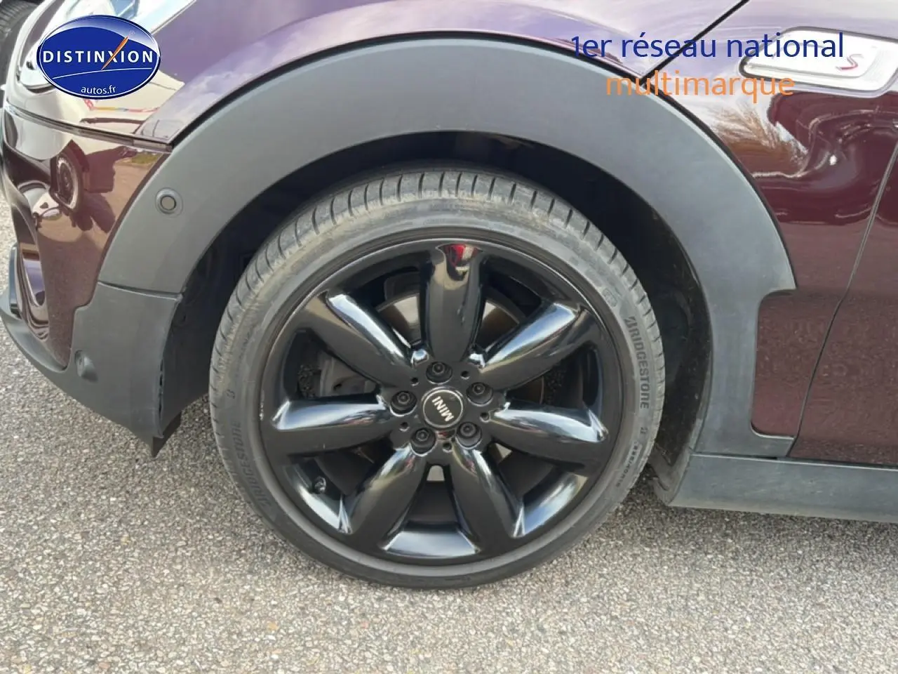 Gros plan sur la roue avant gauche noire brillante d'une MINI Clubman F54 bordeaux, avec logo MINI au centre.