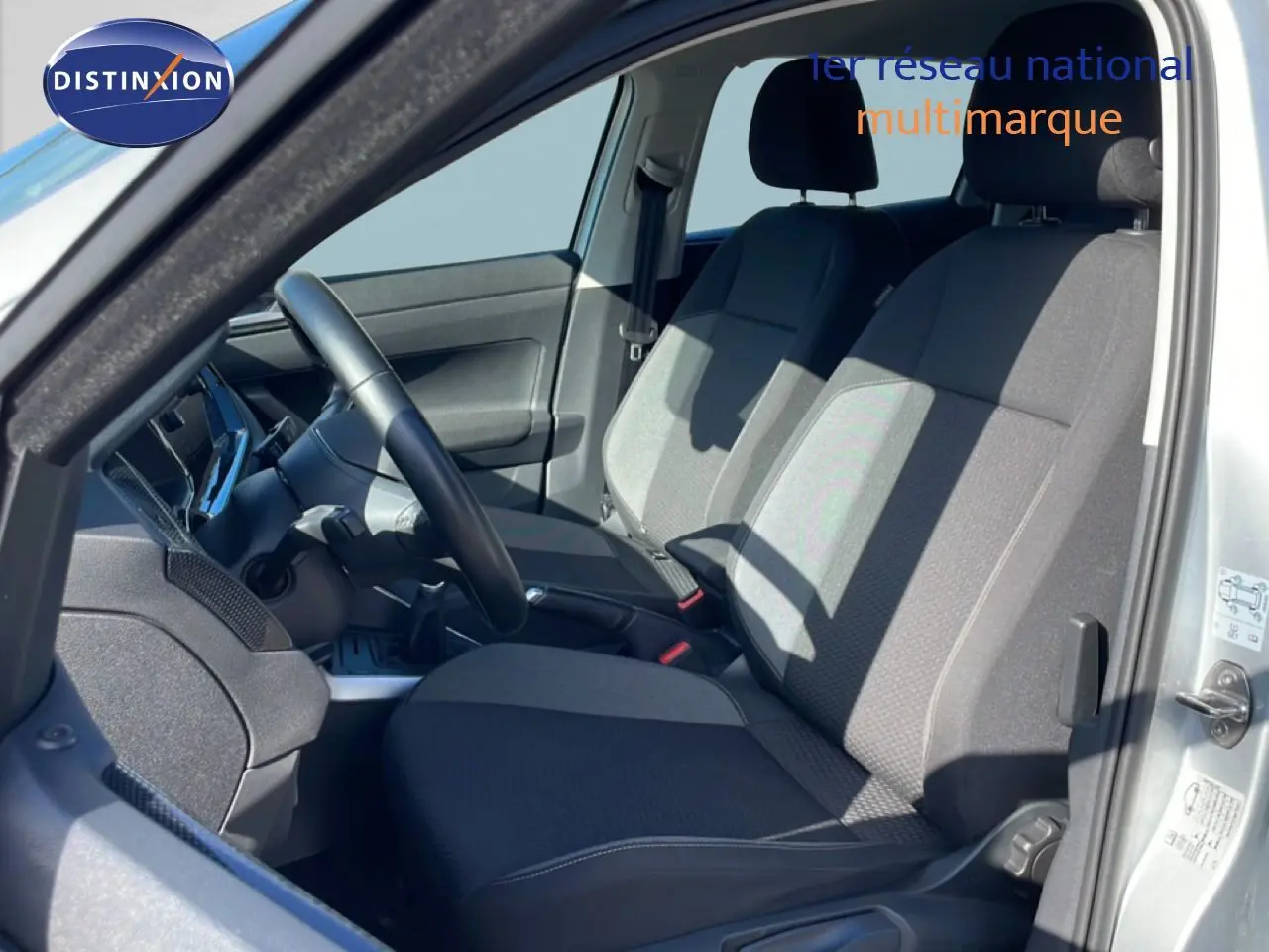 Vue intérieure côté conducteur du Volkswagen Taigo 2022 en reflet d'argent, sièges tissu gris et volant cuir noir.