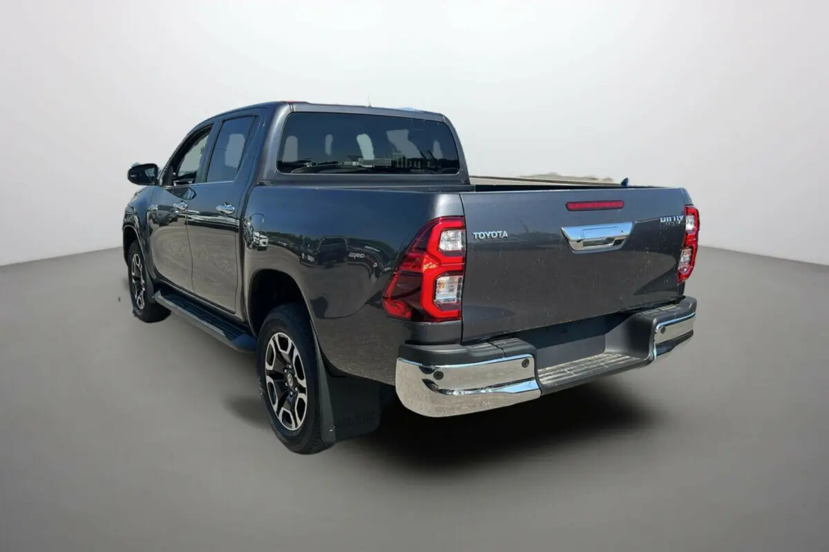 Toyota Hilux 4x4 gris atlas vu 3/4 arrière droit, avec jantes alu 18 pouces et marchepieds chromés.