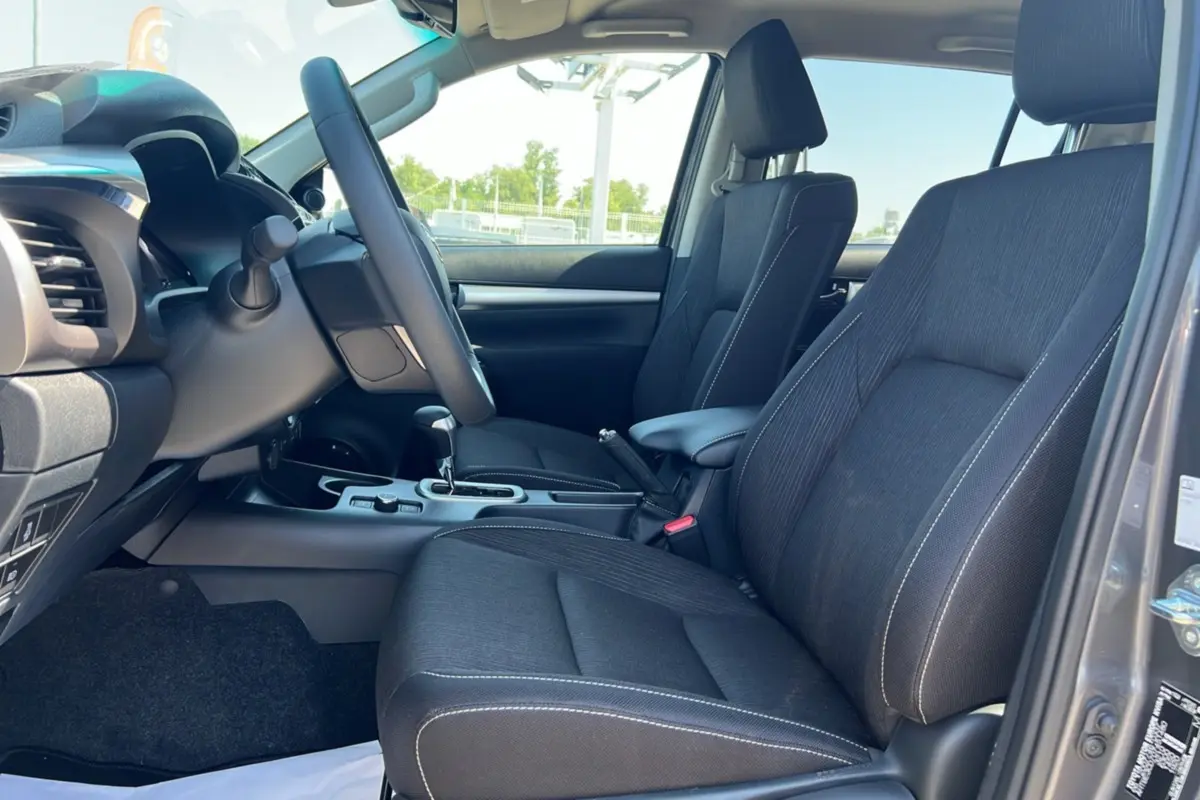 Vue intérieure côté conducteur du Toyota Hilux 2026 gris atlas, sièges tissu noirs avec coutures blanches et console centrale.