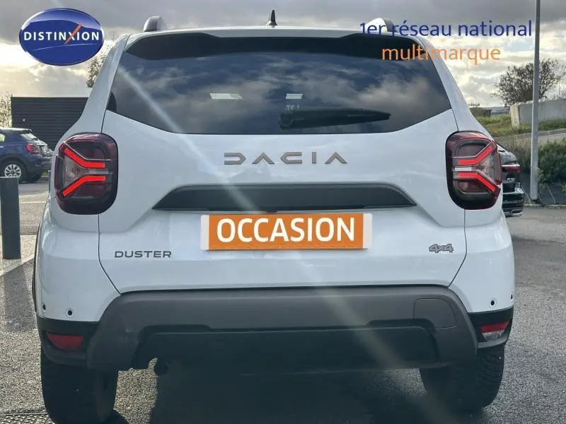 Vue arrière d'un Dacia Duster blanc glacier 2024 avec feux LED caractéristiques et badge 4x4 visible.