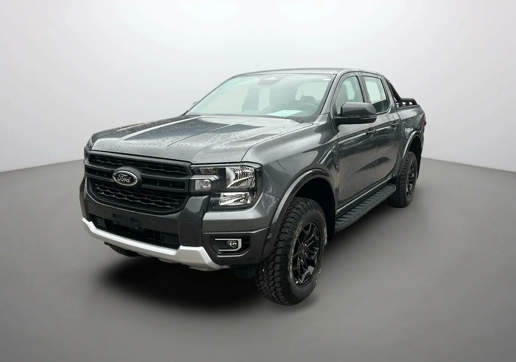 Ford Ranger gris carbone en 3/4 avant droit, avec arceaux noirs et marchepieds visibles sur fond neutre.