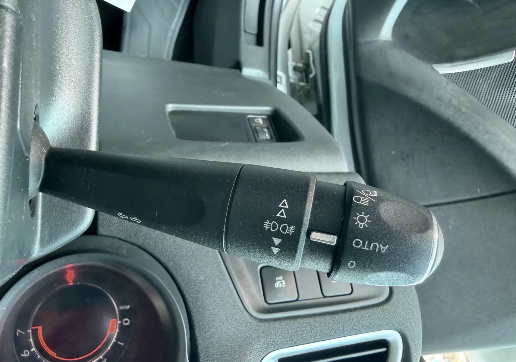 Gros plan sur la commande des phares et clignotants à gauche du volant dans l’habitacle noir d’une Citroën C4 gris.
