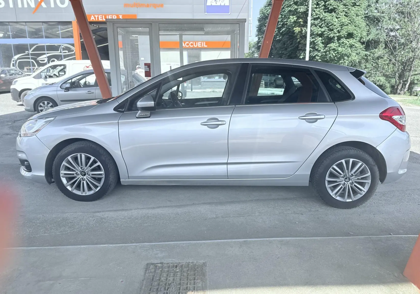 Profil côté gauche d'une Citroën C4 gris clair 5 portes, garée sous un abri avec jantes alliage visibles.