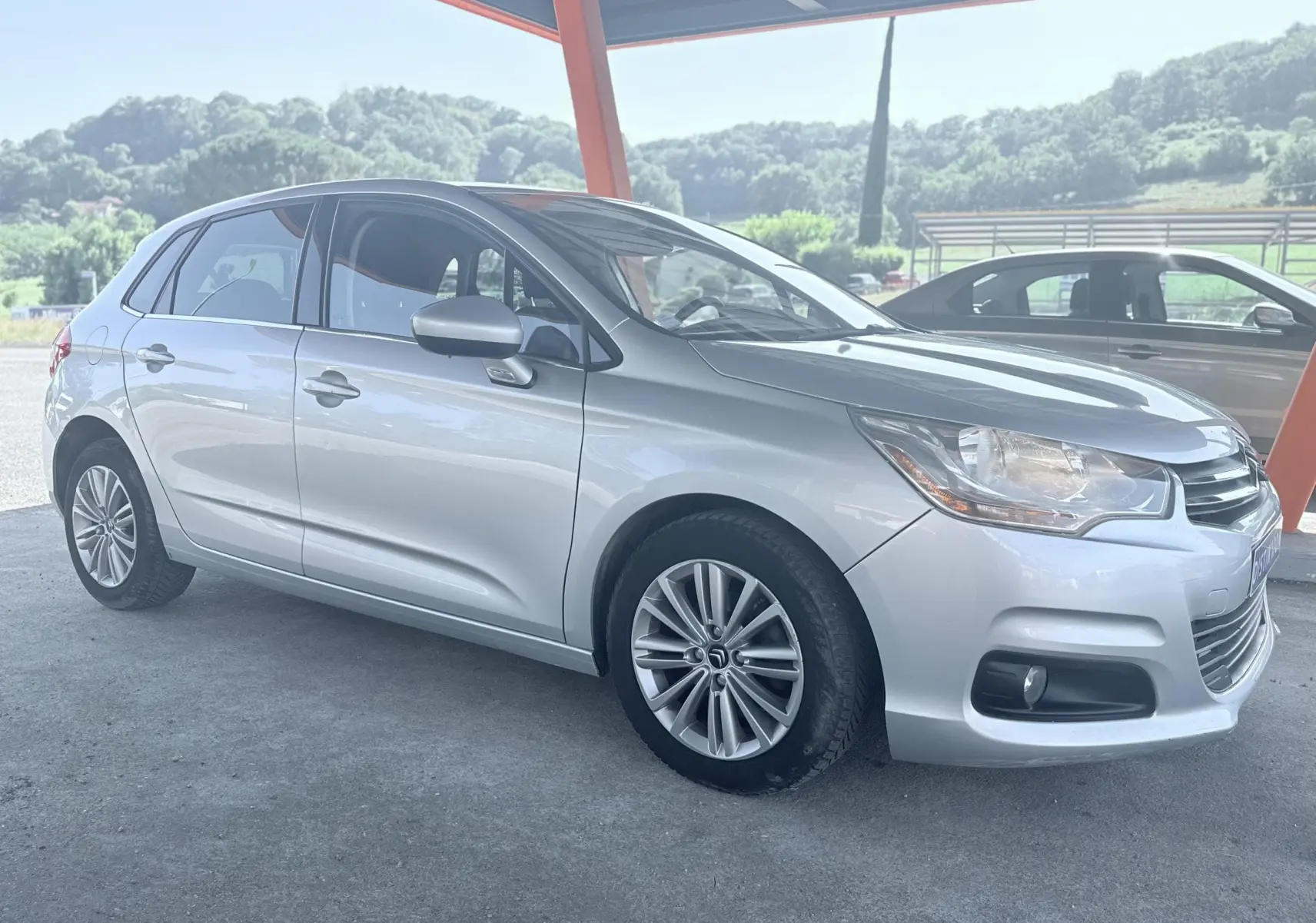 Citroën C4 gris vue 3/4 avant droit, sous abri avec jantes alliage et carrosserie lisse.