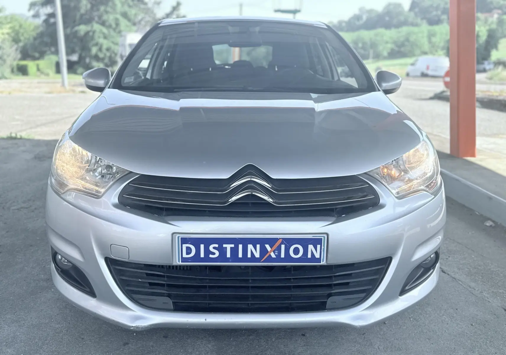 Vue avant d'une Citroën C4 gris métallisé avec phares allumés et plaque d'immatriculation Distinxion.