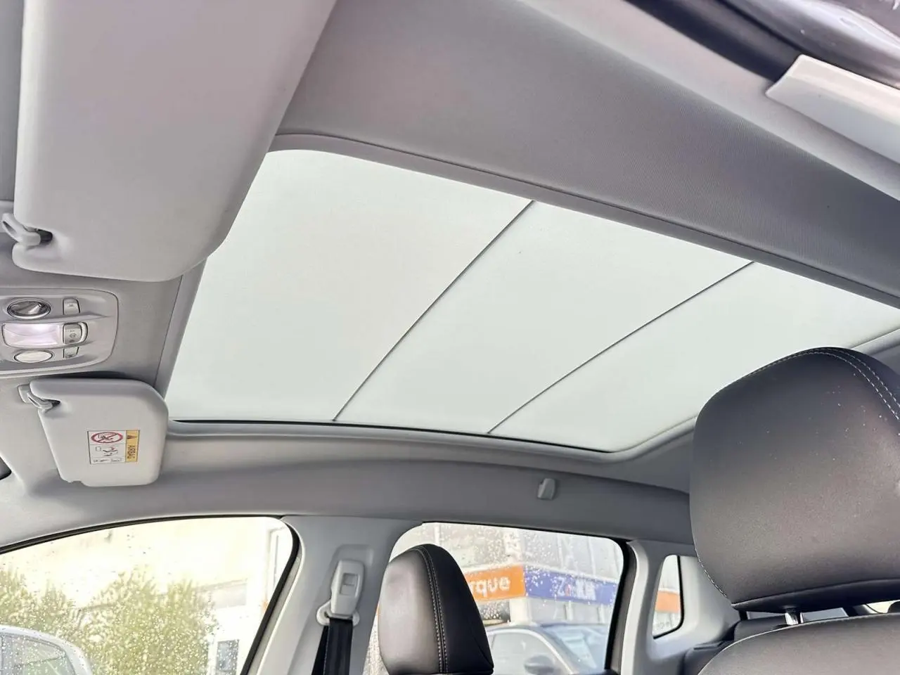 Vue intérieure du toit vitré panoramique avec velum électrique et sièges avant en cuir noir du Peugeot 2008 Crossway gris foncé.