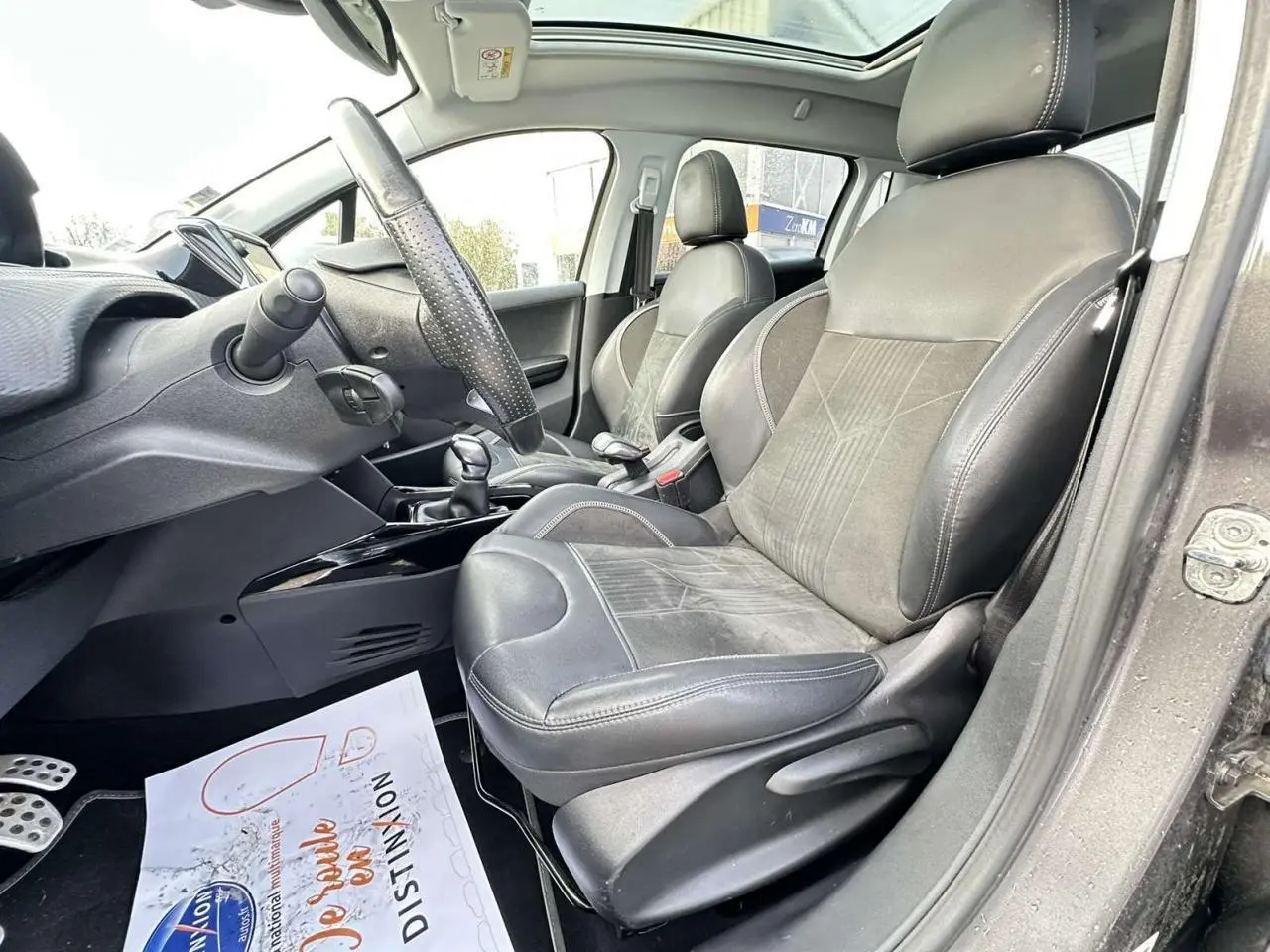 Vue intérieure côté conducteur de la Peugeot 2008 gris foncé, montrant sièges cuir et alcantara, volant et toit panoramique.