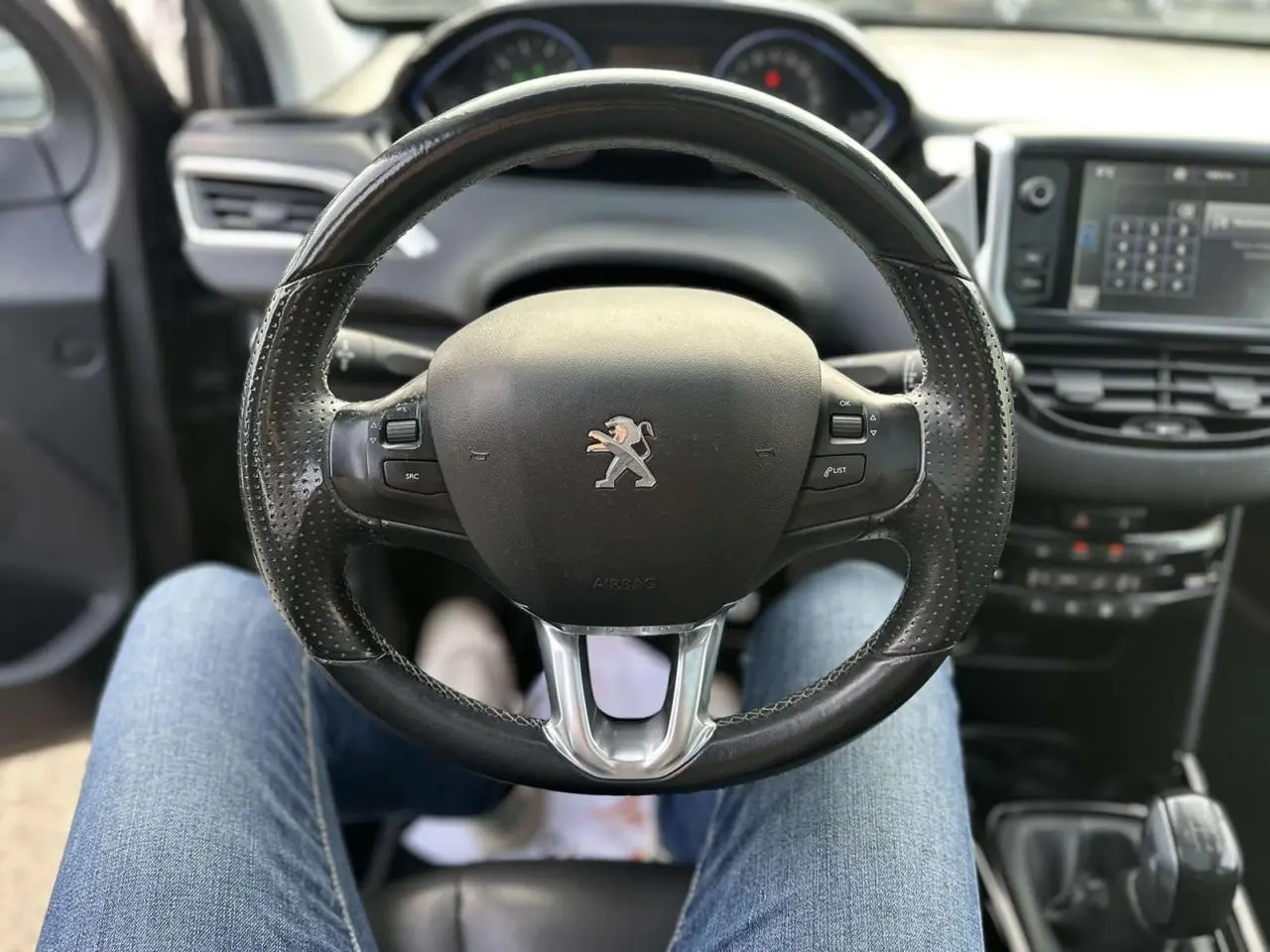 Vue intérieure centrée sur le volant cuir perforé de la Peugeot 2008 gris foncé avec tableau de bord et écran tactile.