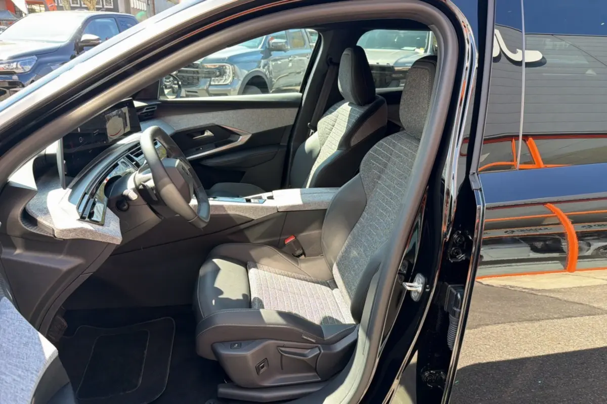 Vue intérieure côté conducteur du Peugeot 5008 Hybrid noir perla nera, sièges en cuir tissu avec réglages électriques visibles.