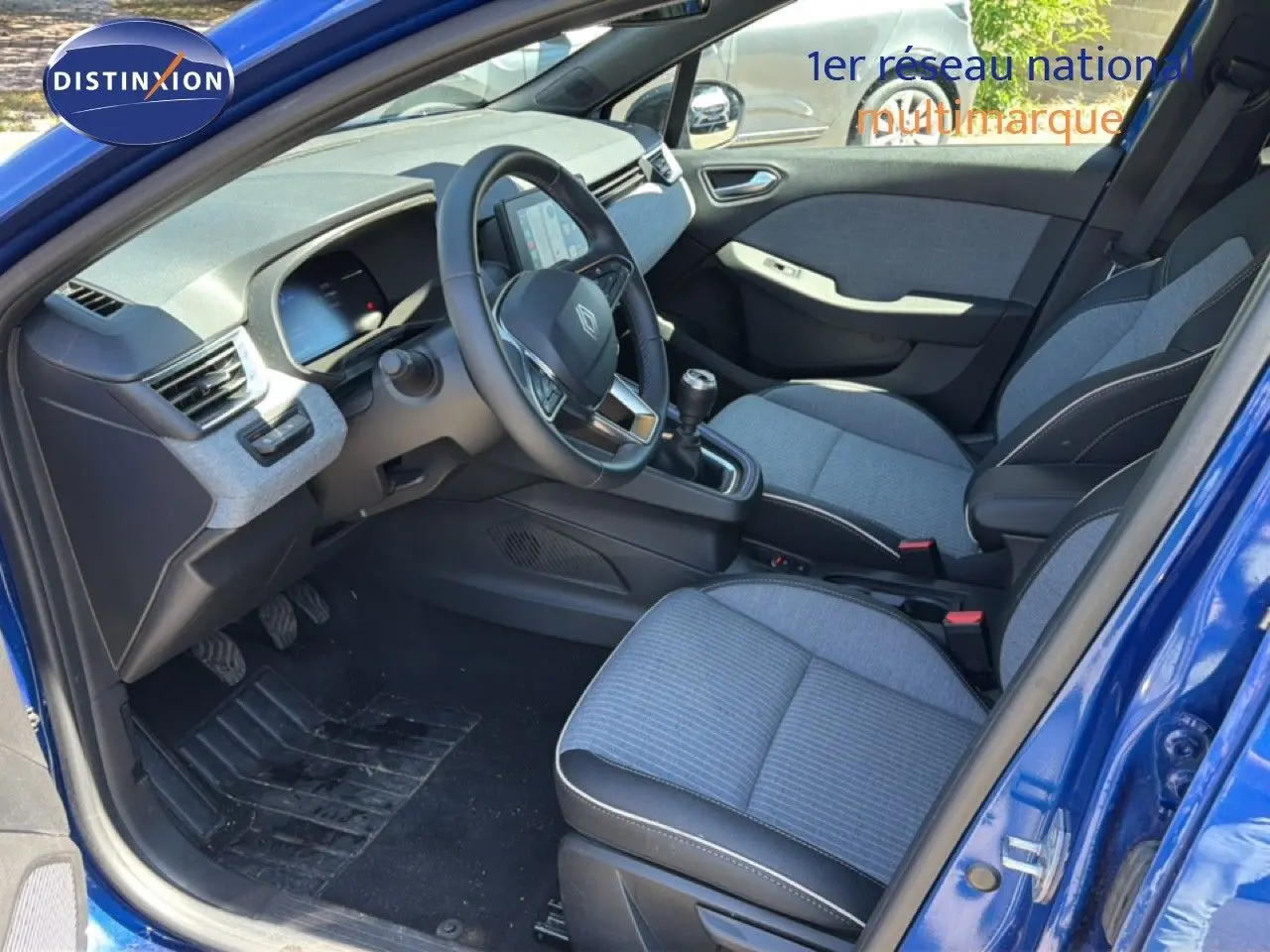 Vue intérieure côté conducteur de la Renault Clio 2025 bleu Iron Metal, avec sièges tissu gris et volant cuir multifonction.