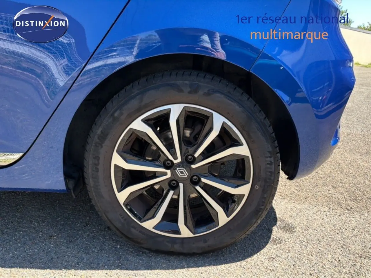 Gros plan sur la roue arrière droite d’une Renault Clio bleu iron metal avec jante alliage bicolore design moderne.