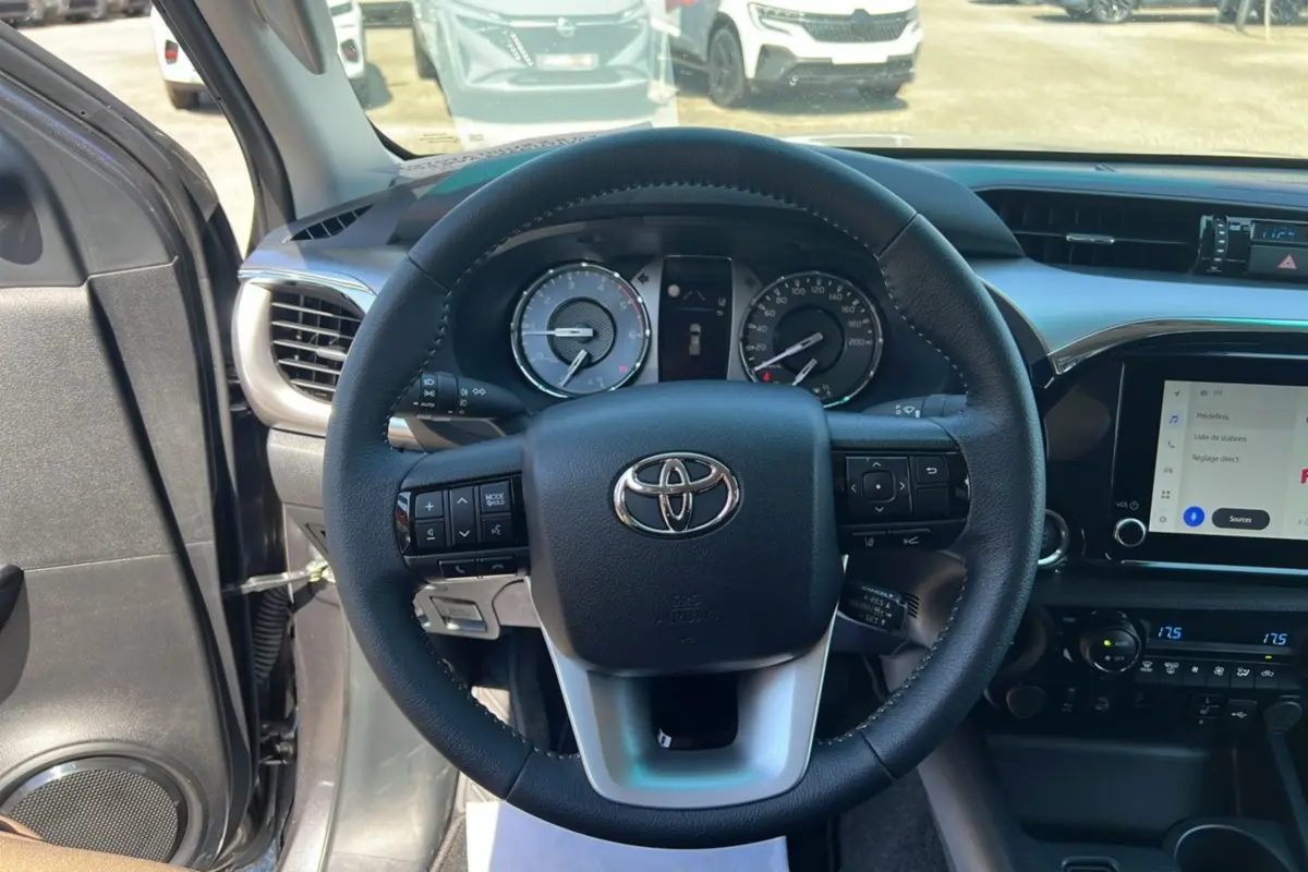 Vue intérieure centrée sur le volant cuir multifonctions du Toyota Hilux 2026, avec tableau de bord et écran tactile visibles.