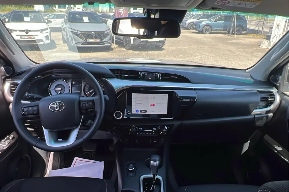 Vue intérieure du tableau de bord du Toyota Hilux 2026, avec volant multifonctions, écran tactile central et commandes de climatisation.