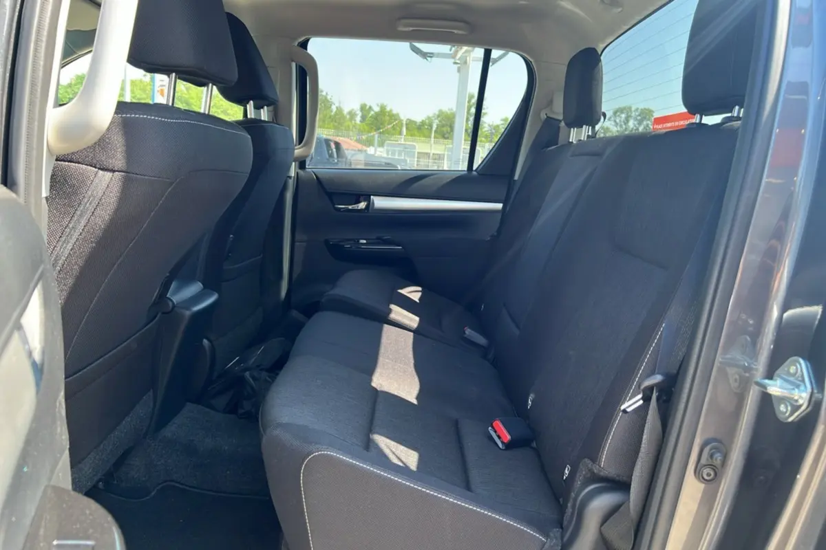 Vue intérieure arrière du Toyota Hilux 2026 gris atlas, montrant la banquette arrière en tissu noir avec ceinture de sécurité rouge.
