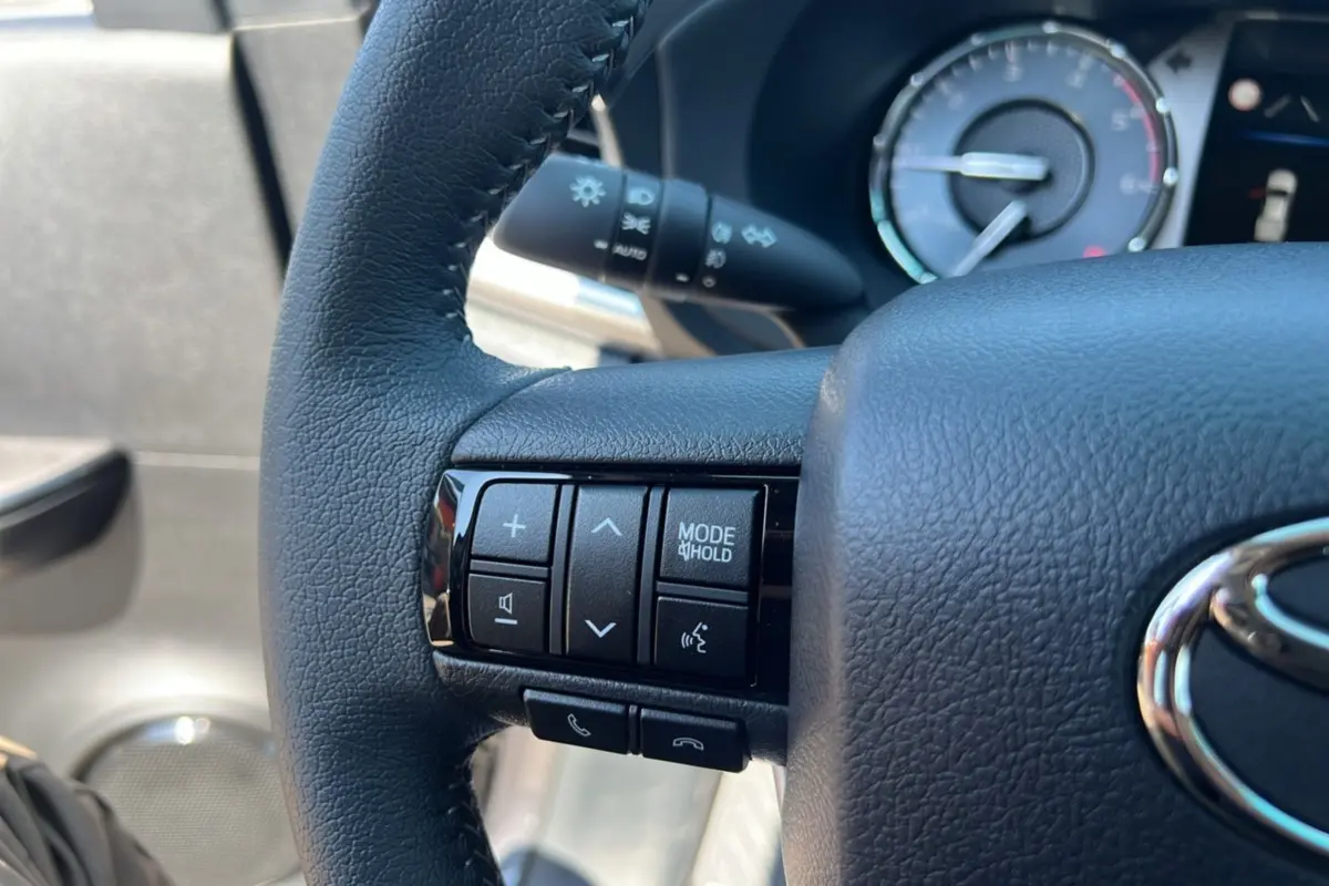 Gros plan sur le volant cuir noir du Toyota Hilux 2026, avec commandes multifonctions et tableau de bord en arrière-plan.