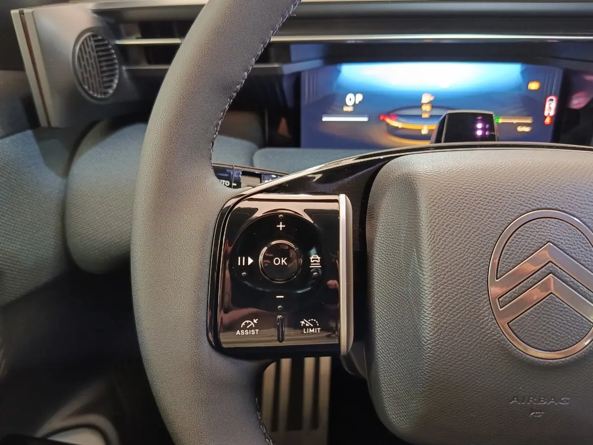 Gros plan sur le volant gris et noir du Citroën C5 Hybride 2026 avec commandes multifonctions et tableau de bord numérique lumineux.