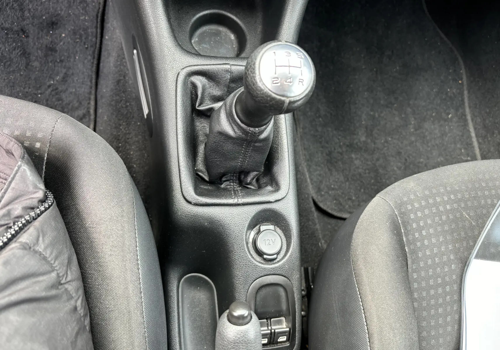 Vue plongeante sur la console centrale d'une Peugeot 206+ gris foncé, mettant en valeur le levier de vitesse manuel et les sièges.