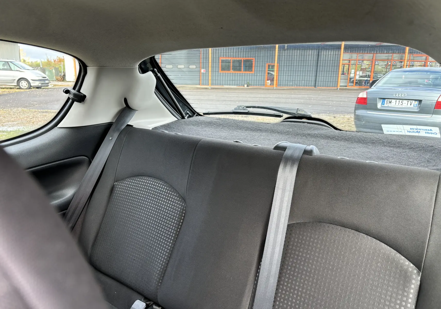 Vue intérieure arrière de la Peugeot 206+ 2009 gris foncé, montrant les sièges arrière et la lunette arrière.