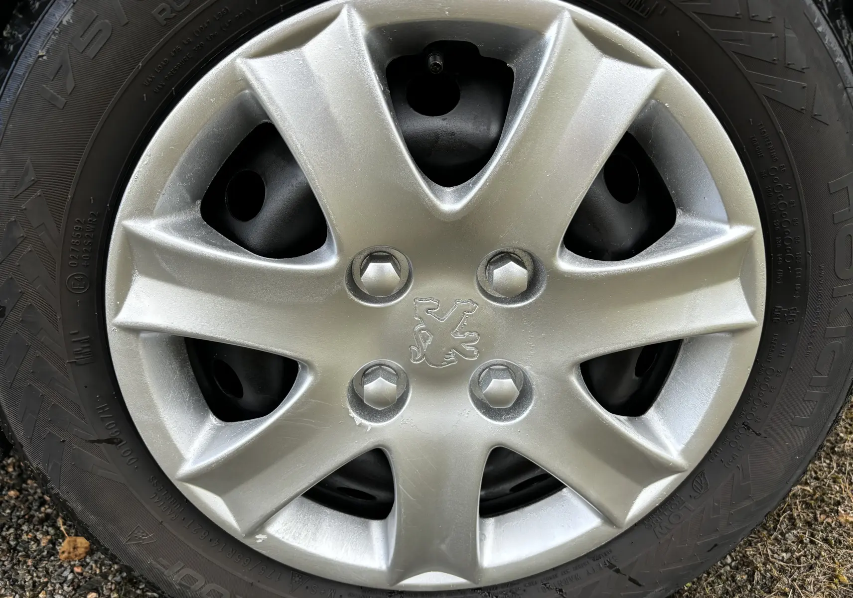Gros plan sur la jante argentée avec le logo Peugeot au centre d’un pneu noir d’une 206+ gris foncé de 2009.