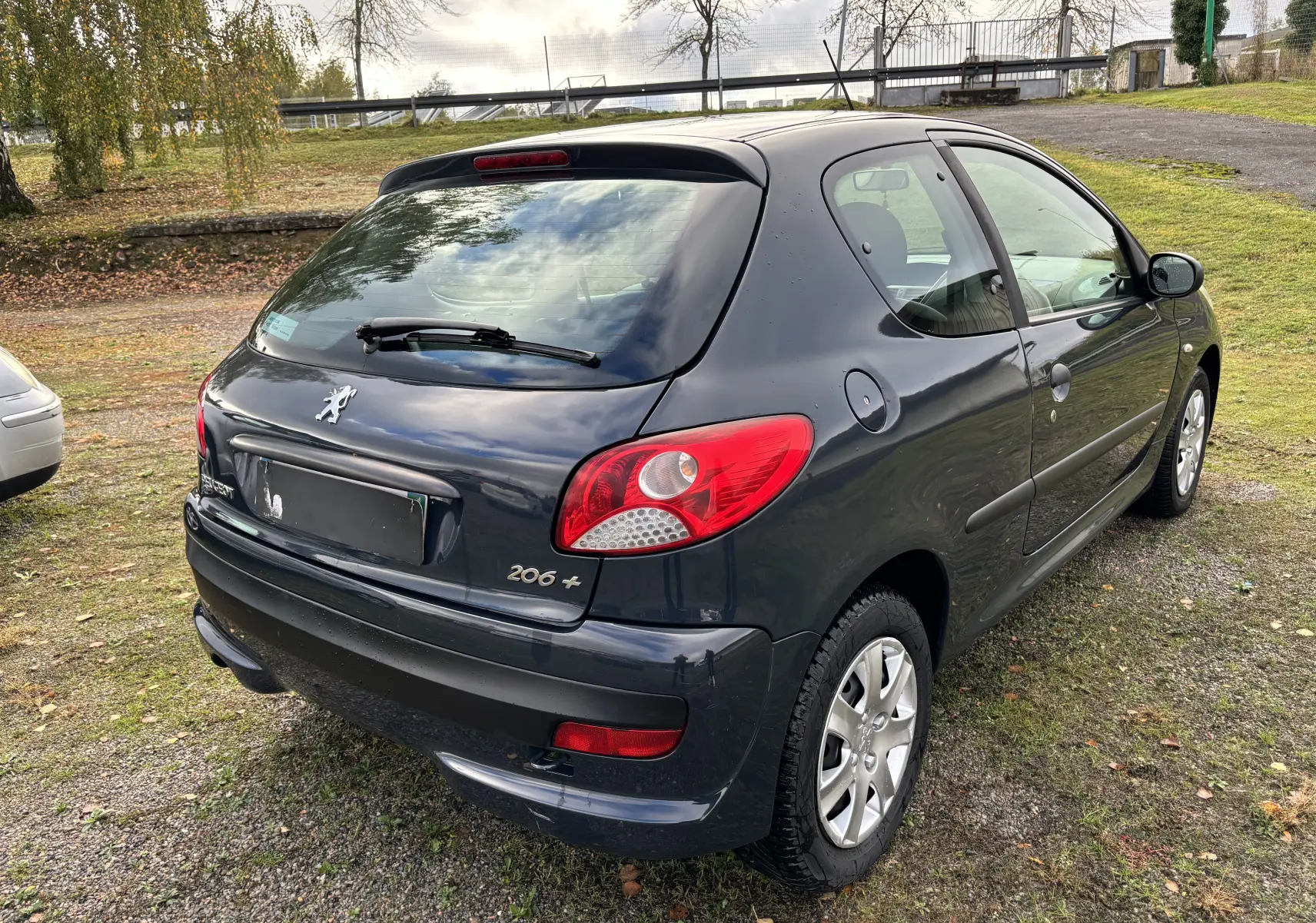 Peugeot 206+ gris foncé vue en 3/4 arrière droit, avec feux arrière rouges et jantes alliage visibles.