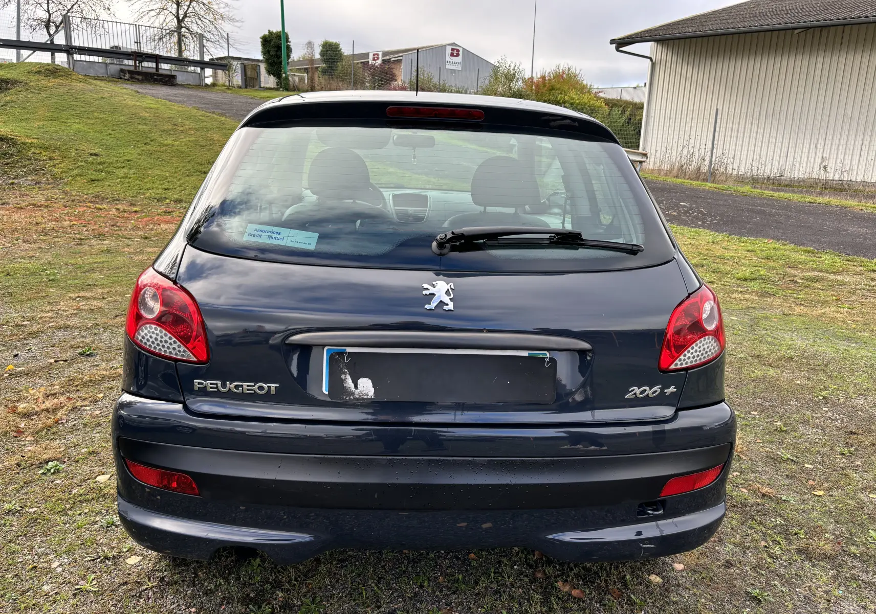 Vue arrière d'une Peugeot 206+ gris foncé de 2009 avec feux rouges et logo lion au centre du hayon.