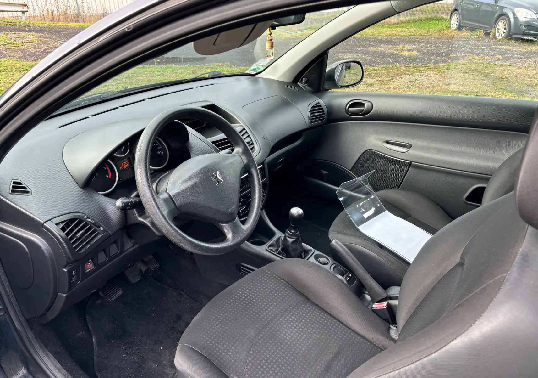 Intérieur côté conducteur d'une Peugeot 206+ gris foncé de 2009, volant, tableau de bord et levier de vitesses manuelle visibles.