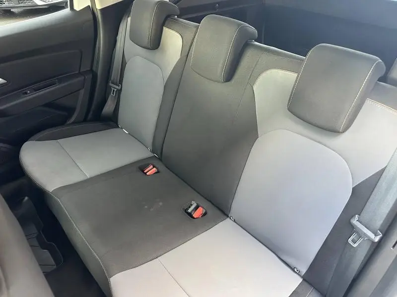 Vue intérieure du siège arrière du Dacia Duster 2024, tissu bicolore gris et noir avec ceintures visibles.