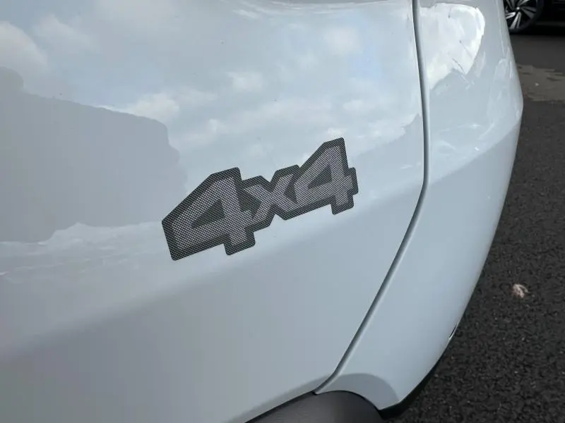 Gros plan sur l'insigne 4x4 en relief gris sur l'aile arrière droite du Dacia Duster blanc Glacier 2024.