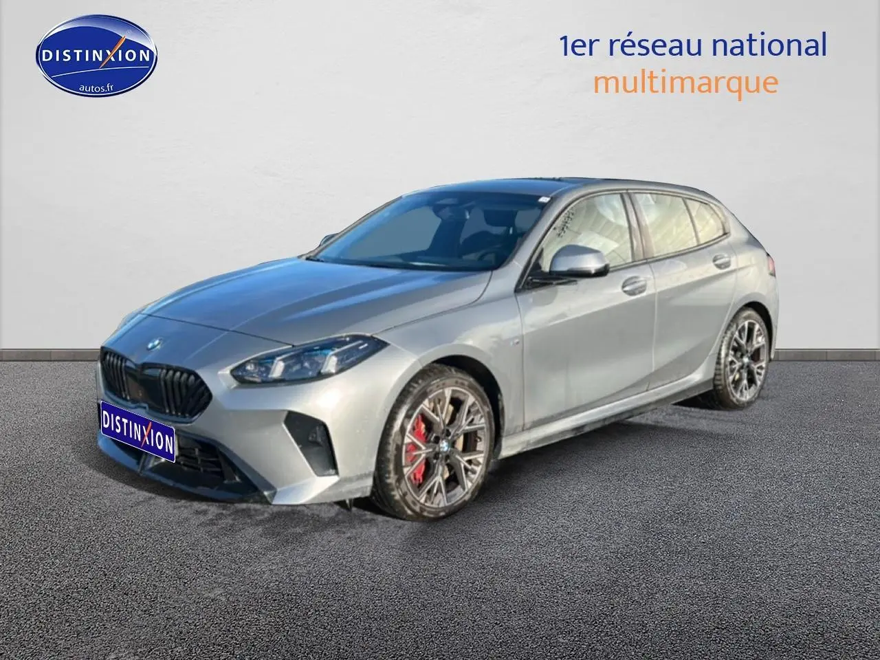 BMW Série 1 118da gris skyscraper vue 3/4 avant droit avec jantes bicolores et étriers rouges visibles.