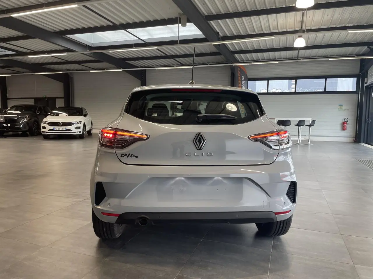 Vue arrière d'une Renault Clio 1.5 Blue dCi 2025 gris Rafale en intérieur avec feux arrière allumés.