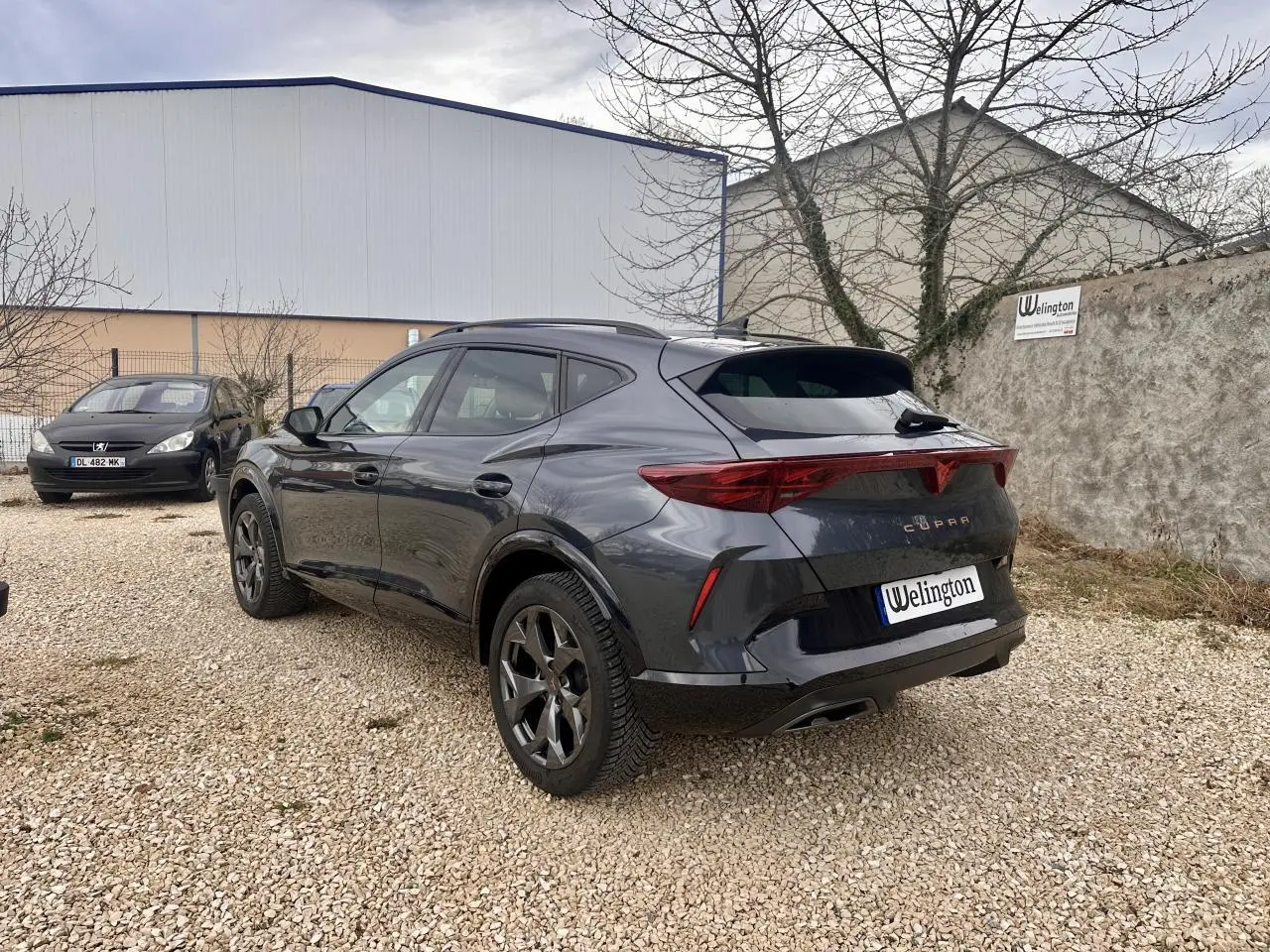 Vue 3/4 arrière droite d'un CUPRA Formentor gris 2025 avec feux arrière triangulaires et jantes noires distinctives.