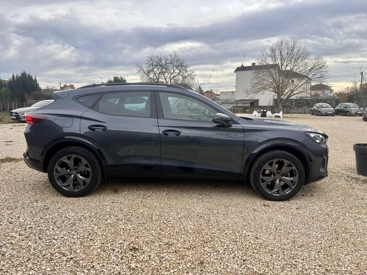 Vue de profil côté gauche d'un CUPRA Formentor gris 2025 avec jantes noires et toit ouvrant.