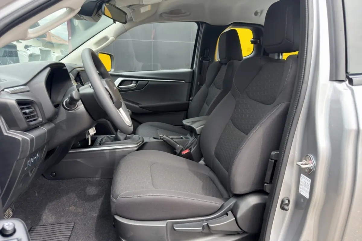 Intérieur côté conducteur de l'Isuzu D-MAX 2026 gris Mercury, sièges tissu noirs avec accoudoir central et volant multifonctions.