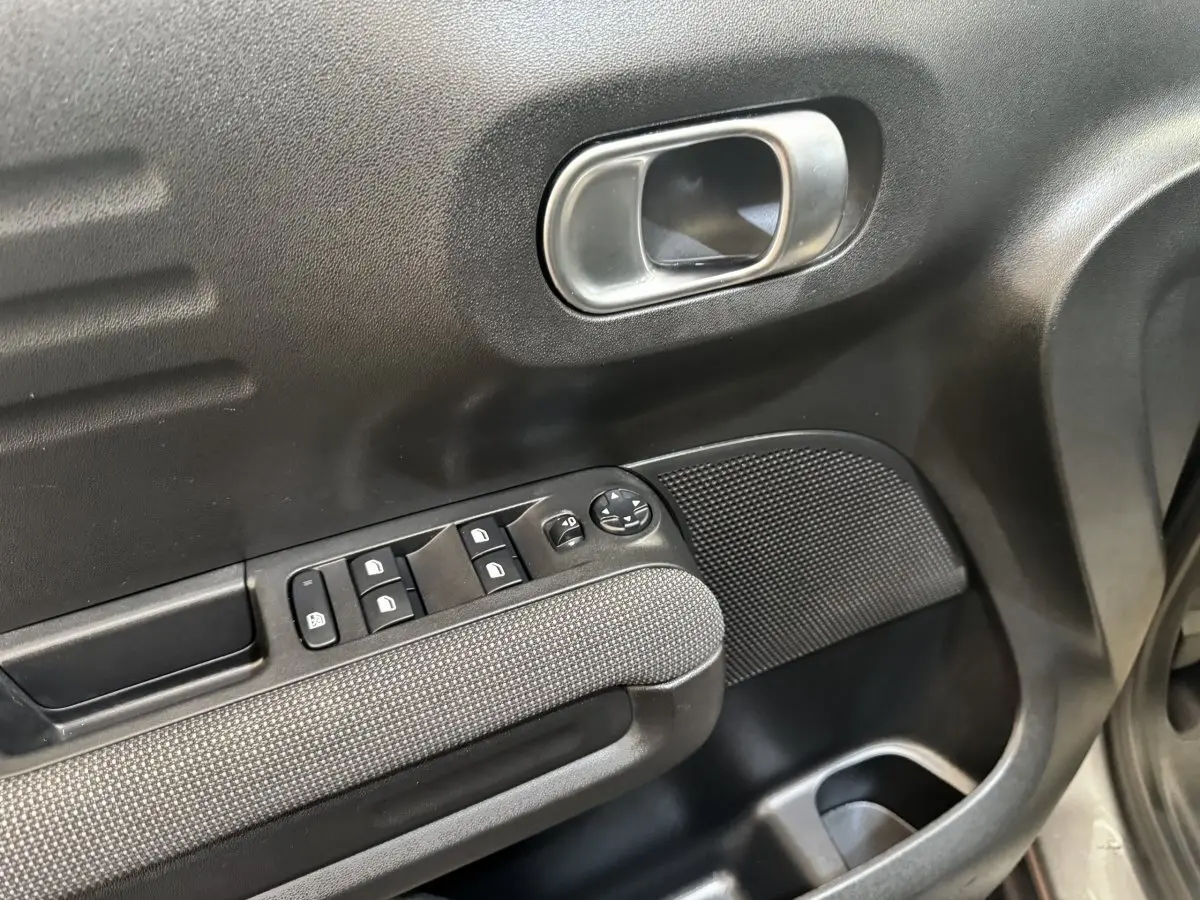 Gros plan sur la porte avant gauche de la Citroën C3 gris foncé, montrant les commandes de vitres et la poignée intérieure chromée.