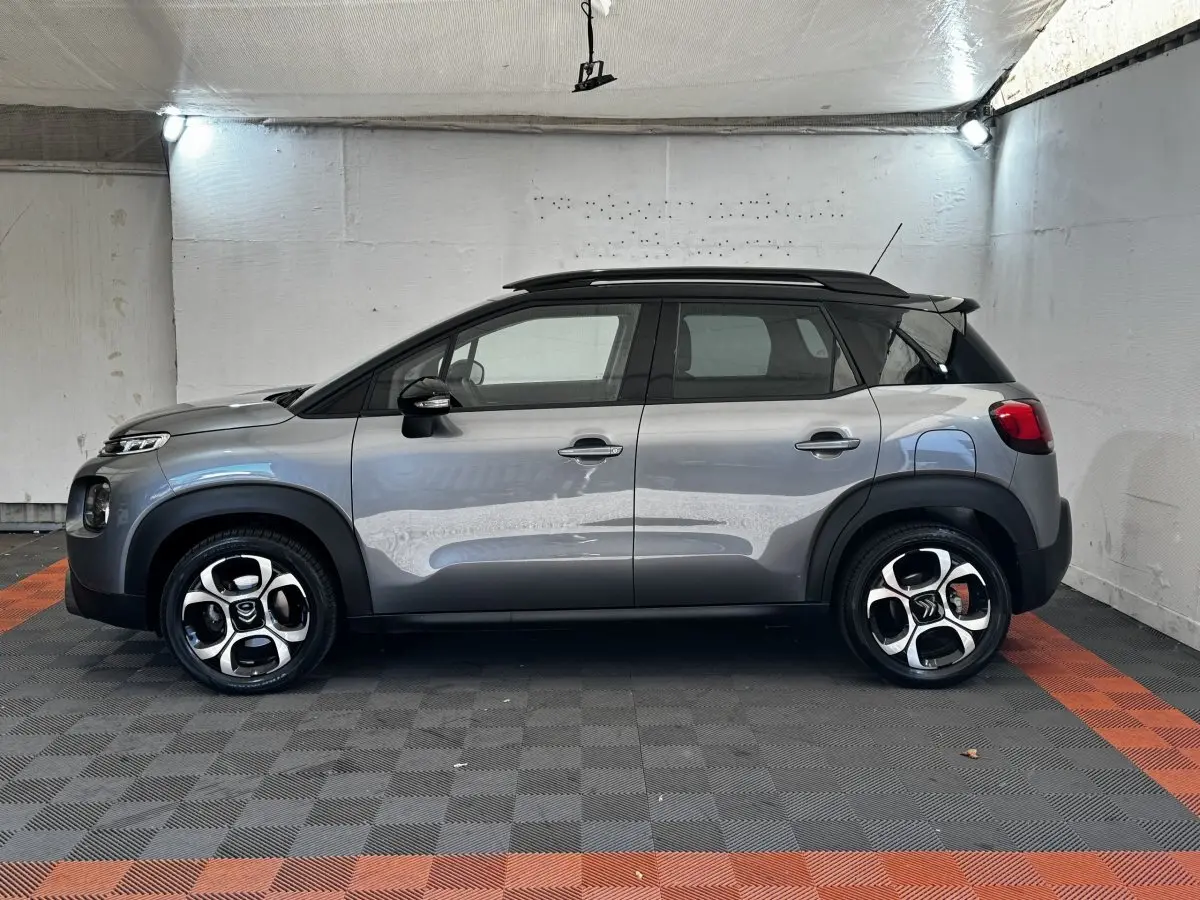 Profil droit d'une Citroën C3 gris foncé 2019 avec toit noir et jantes alliage distinctives en intérieur fermé.