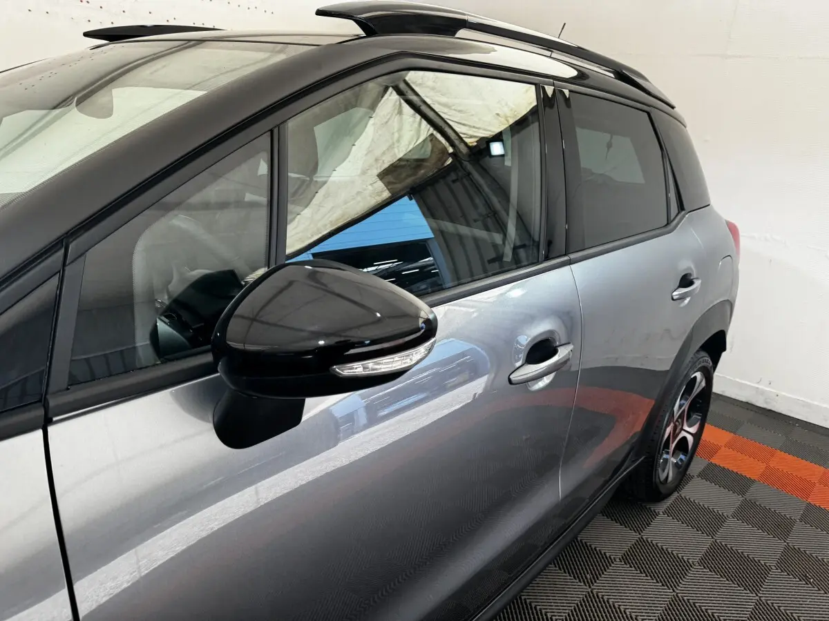 Vue latérale côté gauche d'une Citroën C3 gris foncé avec rétroviseur noir brillant et toit ouvrant partiel visible.