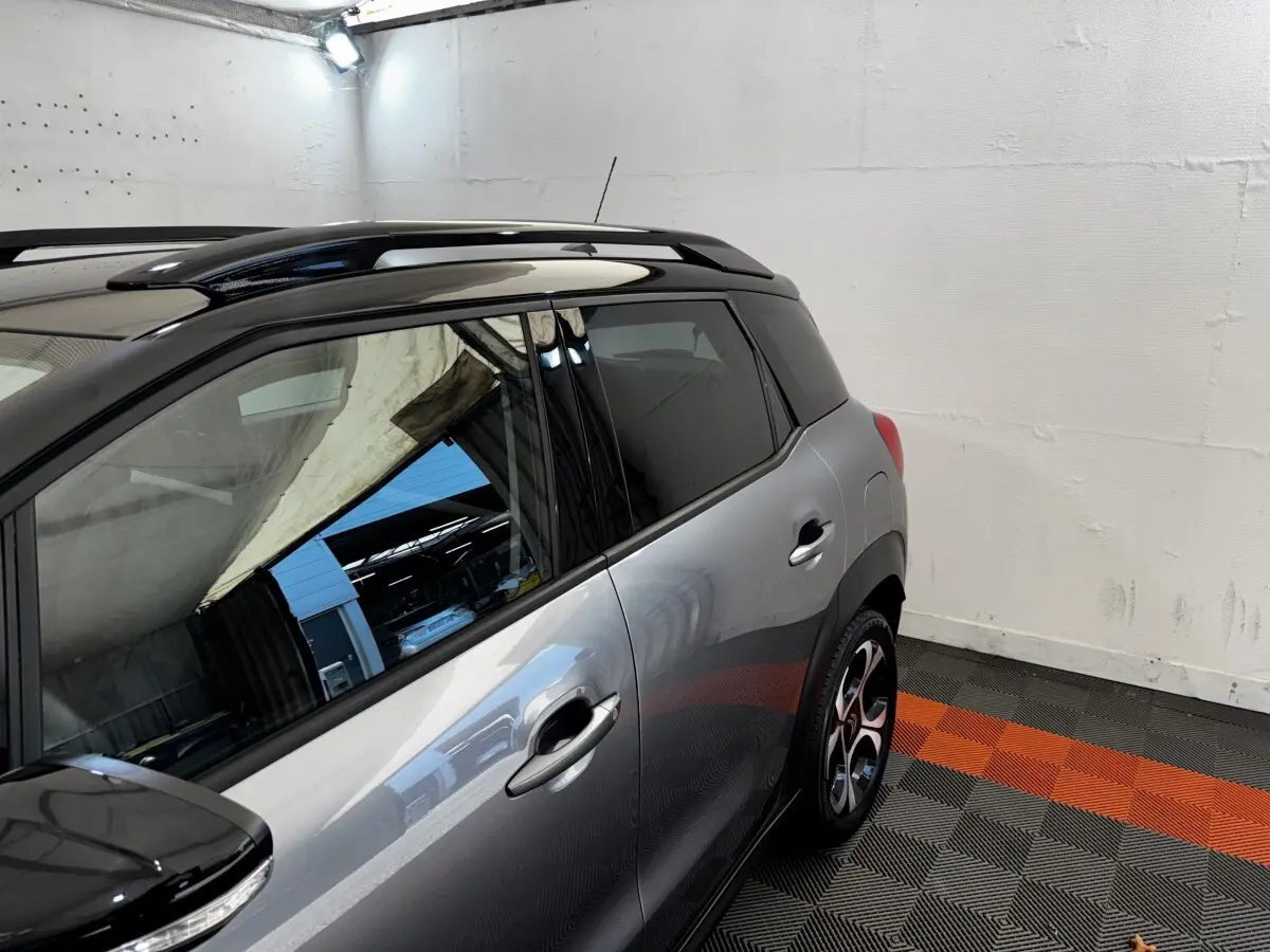 Vue latérale droite d'une Citroën C3 PureTech 110 gris foncé avec toit noir et jantes stylisées en intérieur.