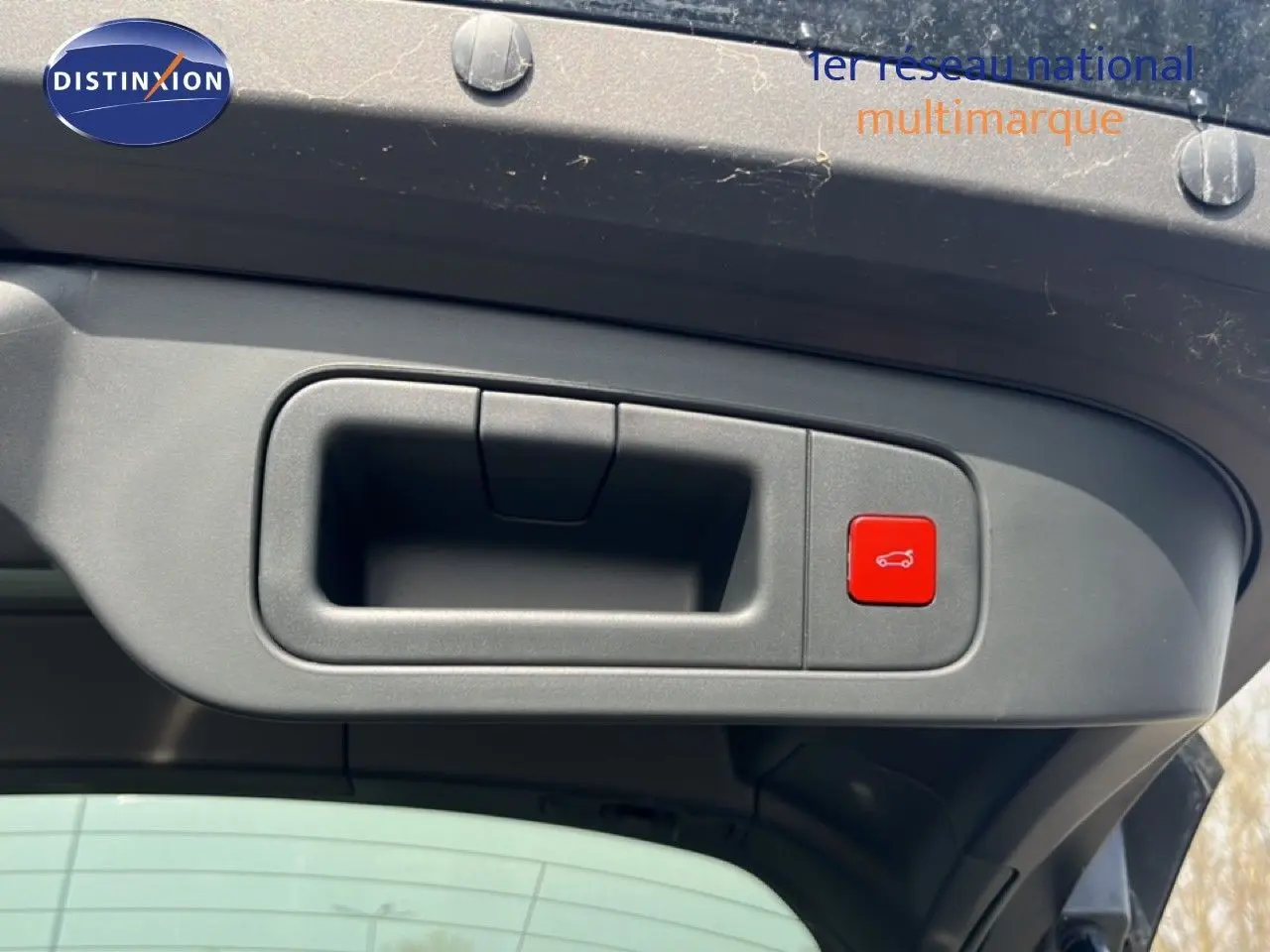Détail de la poignée intérieure et bouton rouge d'ouverture du coffre sur le hayon d'une Citroën C5 X noir métal.