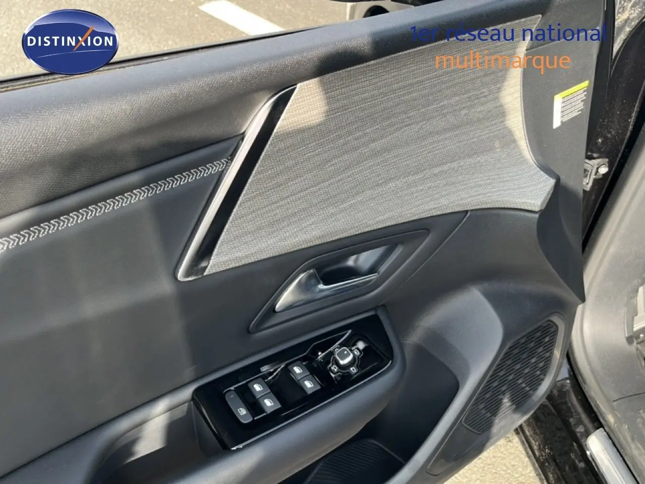 Détail de la porte avant gauche noire métal du Citroën C5 X 2023 avec commandes de vitres et insert tissu gris.