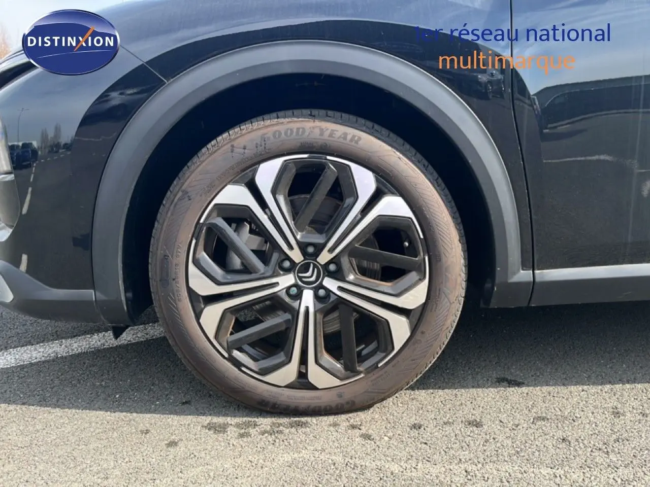 Gros plan sur la roue avant gauche d'une Citroën C5 X noire métallisée avec jante alliage bicolore.