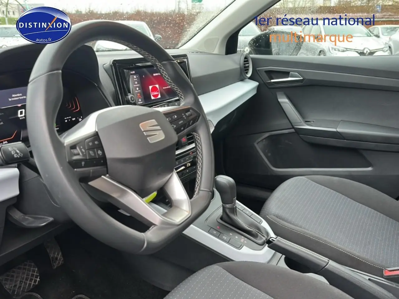 Vue intérieure côté conducteur du SEAT Arona 2025 noir minuit, volant cuir méplat et console centrale avec levier de boîte auto.