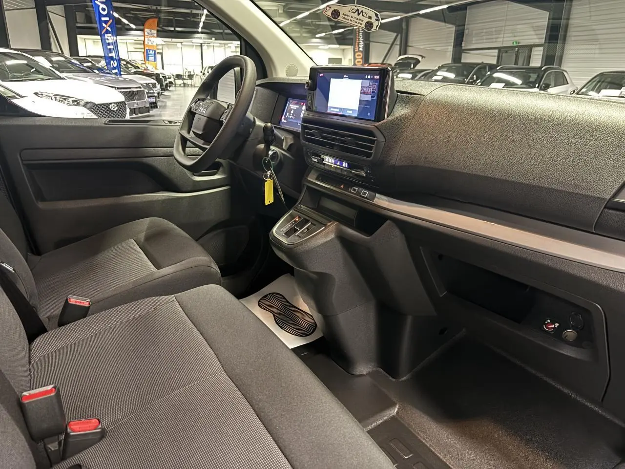 Vue intérieure côté conducteur du Fiat Scudo Fourgon gris foncé, montrant le tableau de bord moderne avec écran tactile et volant multifonction.