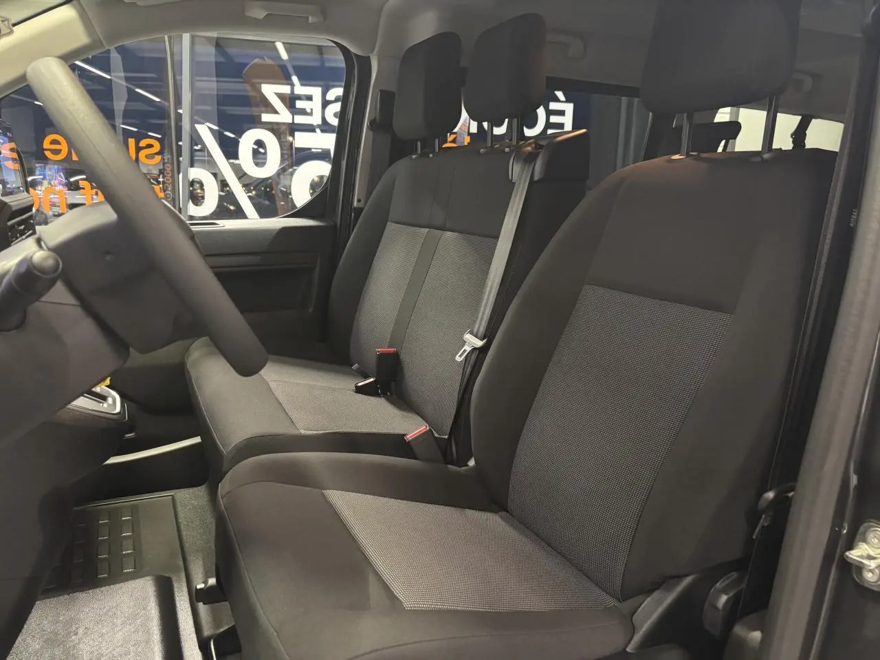 Vue intérieure côté conducteur du FIAT Scudo Fourgon gris foncé, montrant les sièges tissu bi-ton noir et gris.