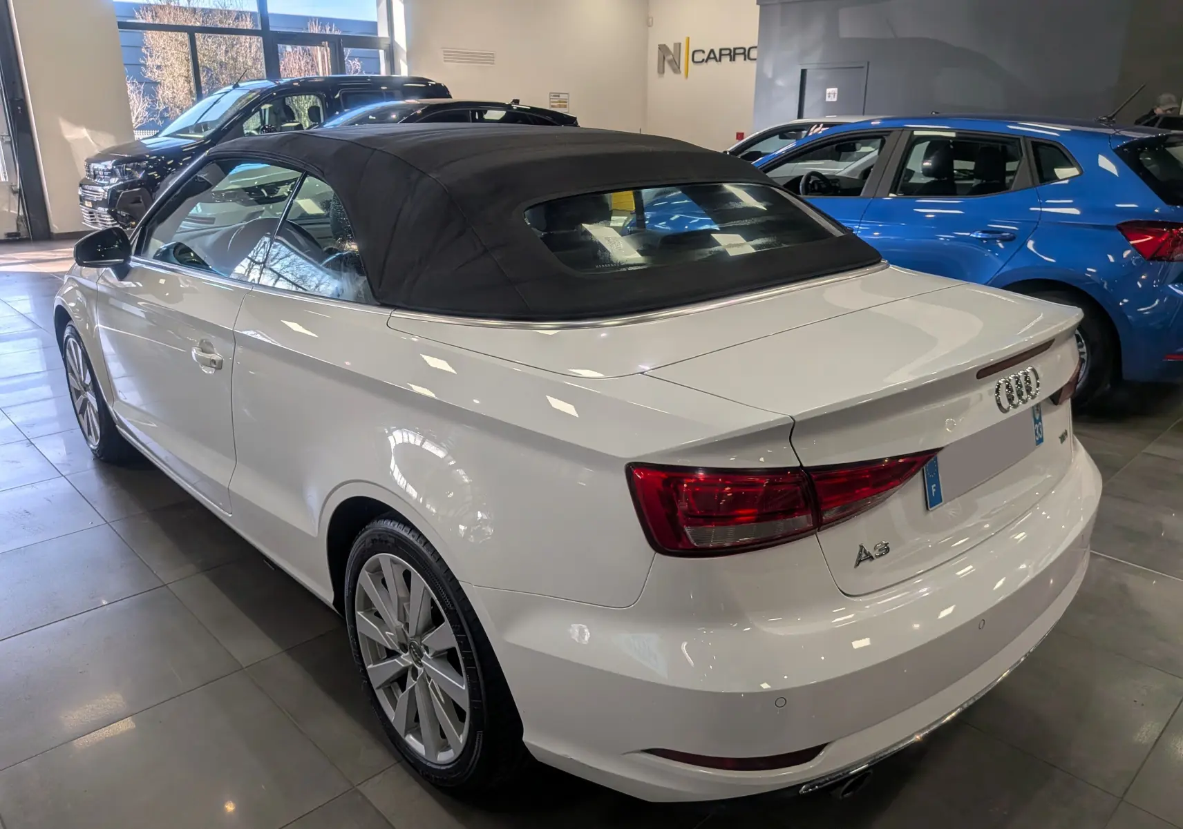 Audi A3 Cabriolet blanc vue 3/4 arrière droit avec toit souple noir dans un showroom lumineux.