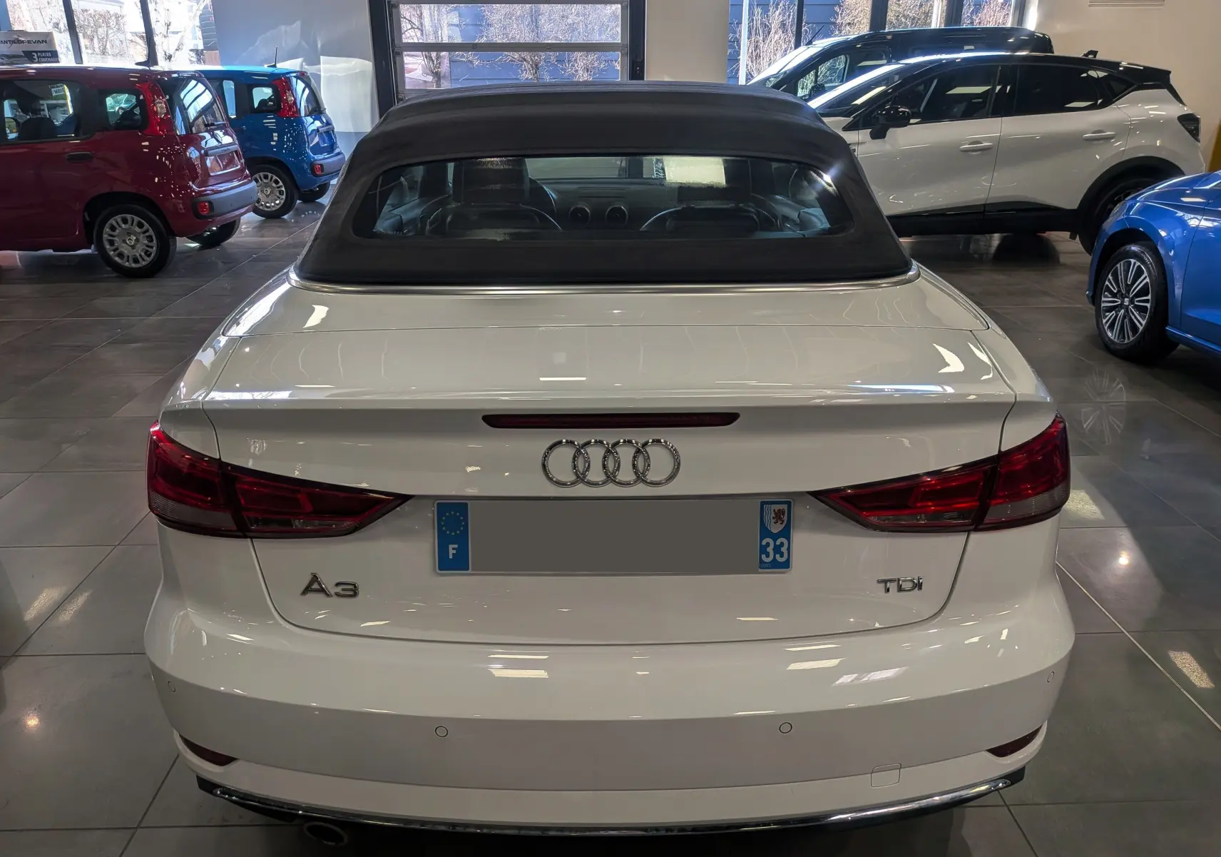 Vue arrière d'une Audi A3 Cabriolet blanche de 2017 avec capote noire, garée en intérieur showroom.